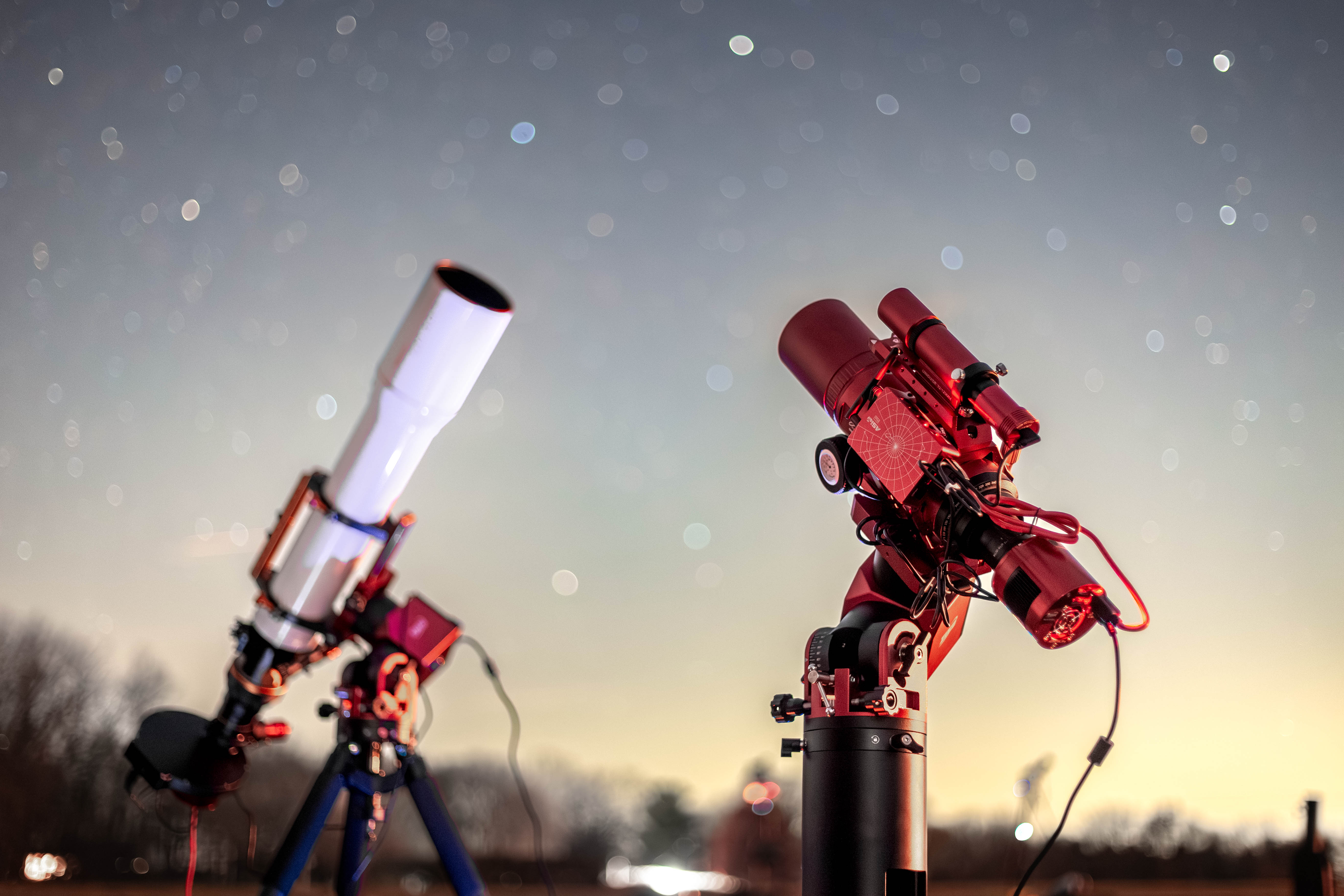 Two telescopes beneath a starry sky, with red light illuminating the equipment.